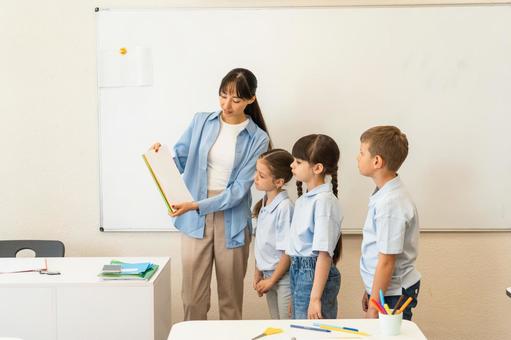 画用紙を見せて説明する女性 女性,女の子,男の子の写真素材