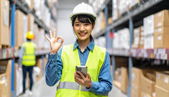 スマホを持ちOKサインの日本人女性作業員 スマホを持ちOKサインの日本人女性作業員の写真