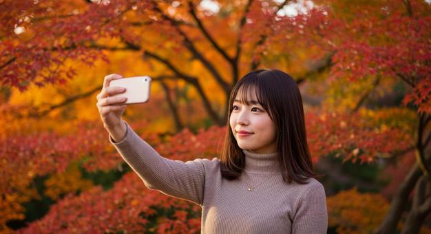 紅葉 深紅の楓を背景に自撮りする若い女性 紅葉 深紅の楓を背景に自撮りする若い女性の写真