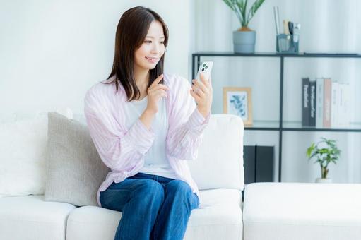 部屋でスマホを操作する若い女性 部屋でスマホを操作する若い女性 スマホ,笑顔,女性の写真素材