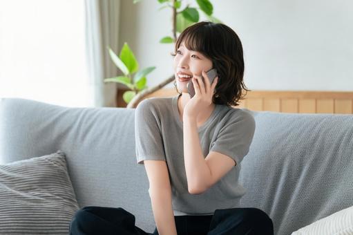 ソファに座ってスマホで話す笑顔の女性 女性,スマホ,スマートフォンの写真素材