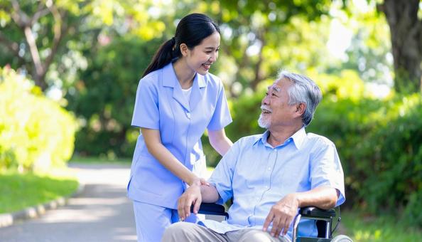 散歩する車椅子の高齢男性と女性介護士の写真