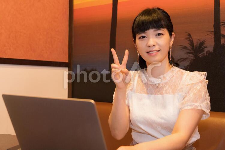 ノートパソコンの前でピースサインする女性 ノートパソコン,ピースサイン,ピースの写真素材