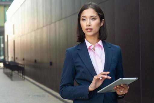 街なかでタブレットを使うスーツのアジア人女性 ビジネスウーマン,ビジネス,女性の写真素材