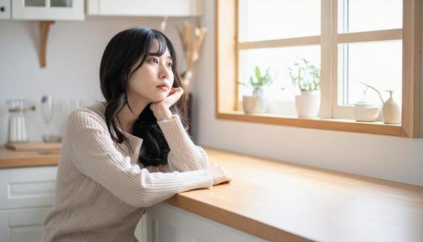 疲れた表情でキッチンに座る若い女性 疲れた表情でキッチンに座る若い女性の写真