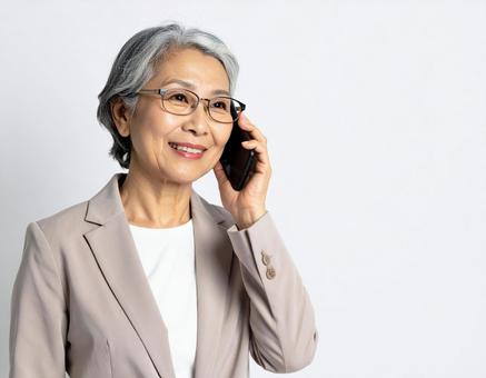 携帯電話で通話をする年配のスーツ姿の女性 携帯電話で通話をする年配のスーツ姿の女性の写真