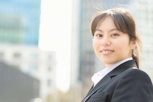 ビル街でカメラ目線のスーツの女性 ビル街でカメラ目線のスーツの女性 日本人,女性,20代の写真素材