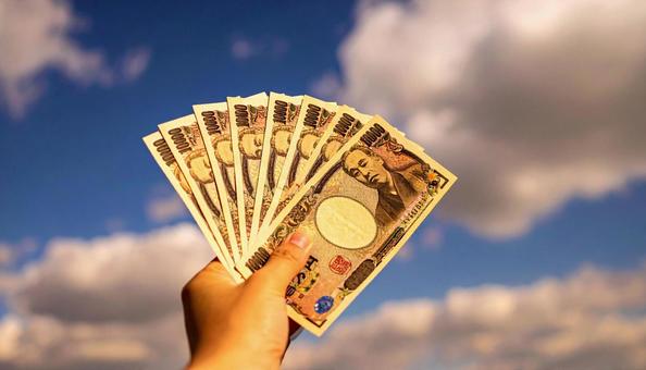 一万円を持つ手 青空背景 一万円を持つ手 青空背景の写真