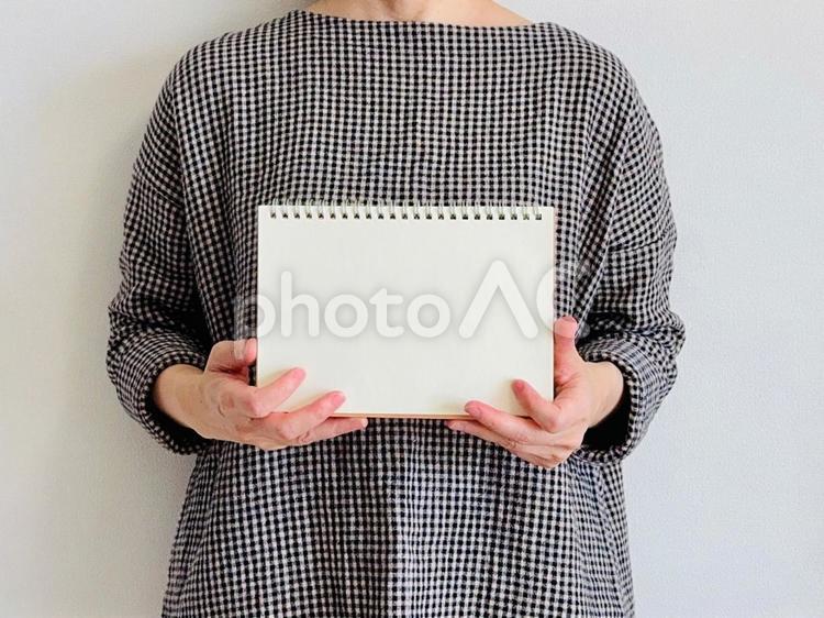 ノートを両手で持つチェック柄の服の女性 ノート,メッセージ,お知らせの写真素材