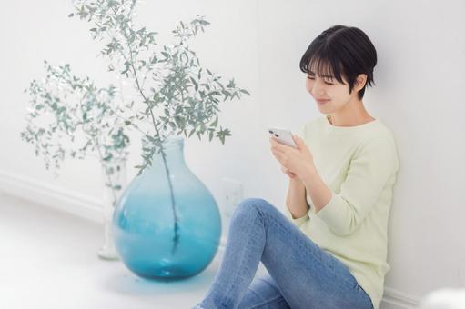 壁に寄り掛かりスマートフォンを使う女性 壁に寄り掛かりスマートフォンを使う女性の写真