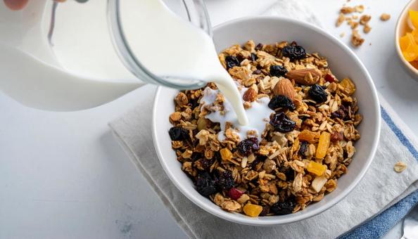 ドライフルーツ入りグラノーラに牛乳を注ぐ ドライフルーツ入りグラノーラに牛乳を注ぐの写真