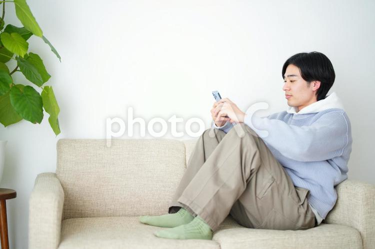 ソファの上に横向きに座ってスマートフォンを見ている男性 引っ越し,一人暮らし,男性の写真素材