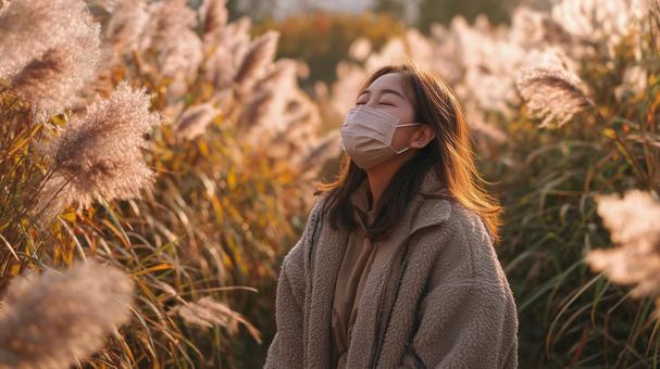 秋風に揺れるススキとマスク姿の女性の写真