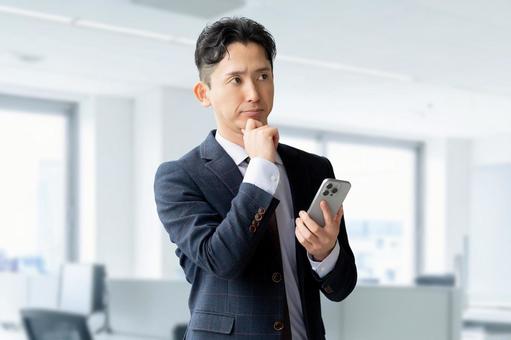 スマホを持って考える男性ビジネスマン 男性,ビジネス,ビジネスマンの写真素材
