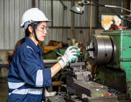 工場で加工機械で金属加工する女性スタッフの写真