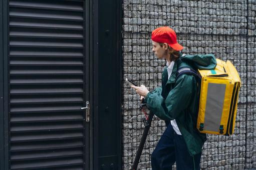 家の門の前でスマートフォンを使うフードデリバリーの男性 配達,フードデリバリー,デリバリーの写真素材
