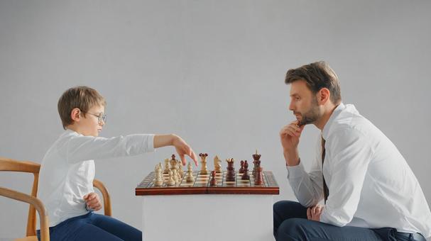 向かい合いチェスをしている男の子とお父さん(グレー背景) 向かい合いチェスをしている男の子とお父さん(グレー背景) チェス,親子,お父さんの写真素材