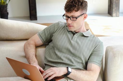 ソファで膝の上でノートパソコンを使っている男性 男性,外国人,欧米人の写真素材