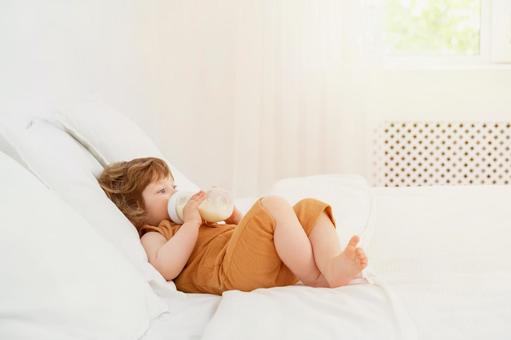 ベッドで寝転びミルクを飲む子供 ベッドで寝転びミルクを飲む子供 赤ちゃん,哺乳瓶,ミルクの写真素材