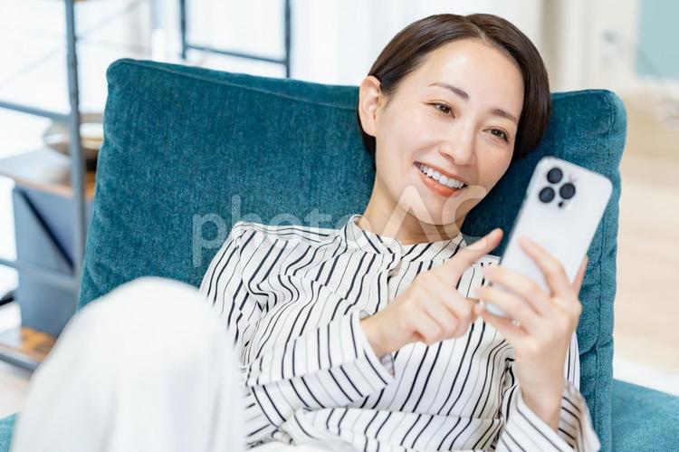 寝転がって携帯を触る女性 スマホ,ビジネス,メッセージの写真素材