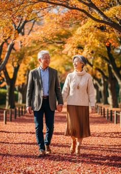 手をつなぎ紅葉道を散策するシニアカップル 手をつなぎ紅葉道を散策するシニアカップルの写真
