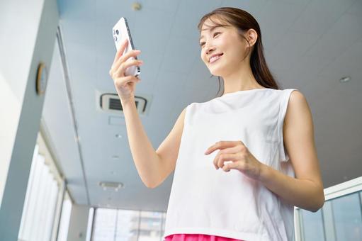 ジムでスマホを操作する女性　トレーニング スポーツジム,スマホ,女性の写真素材