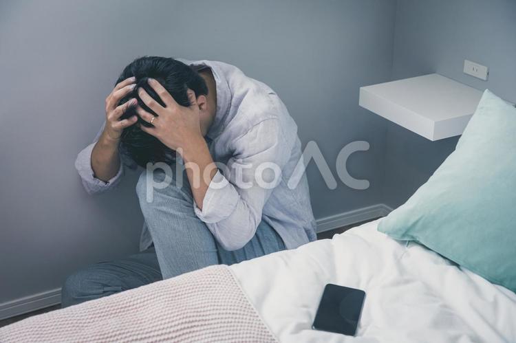 ベッド脇で頭を抱える男性　 一人,孤独,部屋の写真素材