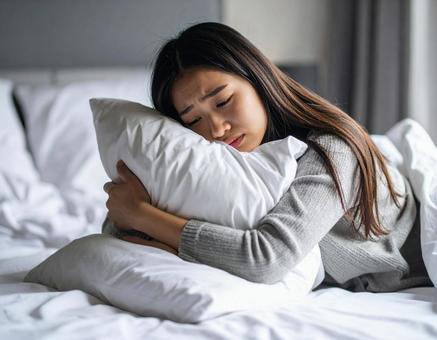 枕を抱きしめて泣く女性(孤独・感情) 枕を抱きしめて泣く女性(孤独・感情)の写真