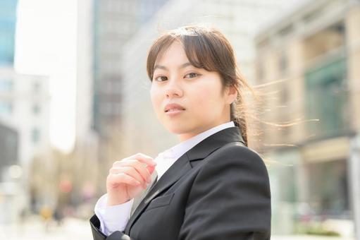 ビル街でカメラ目線のスーツの女性 ビル街でカメラ目線のスーツの女性 日本人,女性,20代の写真素材