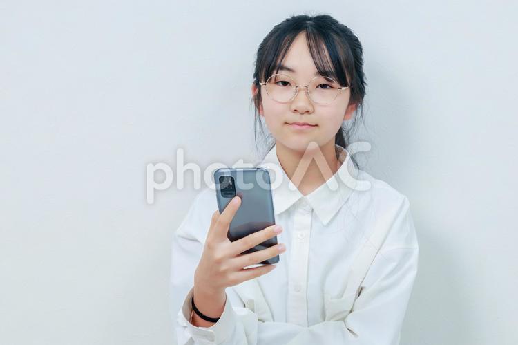 スマホを片手にカメラ目線で微笑む女性 女性,小学生,少女の写真素材