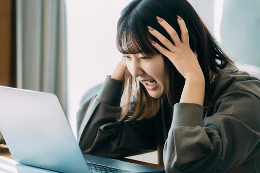 パソコンを使いながら頭を押さえて悩む女性 女性,困る,ショックの写真素材