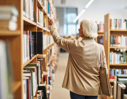 図書館で本を探しているシニア女性 図書館で本を探しているシニア女性の写真