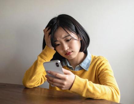 スマホを見て悩む女性の写真