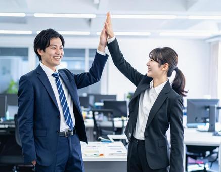 職場でハイタッチして喜ぶ男性と女性の写真