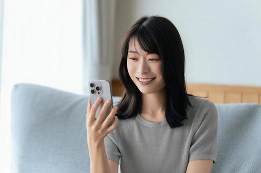 ソファに座ってスマホを使う笑顔の女性 ソファに座ってスマホを使う笑顔の女性 女性,スマホ,スマートフォンの写真素材