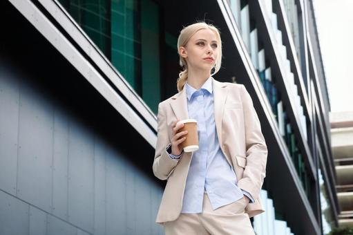 オフィスビルの外でコーヒーを持って立つ外国人女性 ビジネスウーマン,ビジネス,女性の写真素材