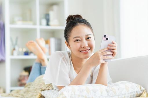 リビングでスマホを見る若い女性 リビングでスマホを見る若い女性 スマートフォン,笑顔,女性の写真素材
