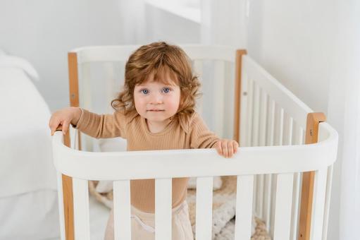 カメラ目線でベッドに立つくせ毛の子供 カメラ目線でベッドに立つくせ毛の子供 赤ちゃん,かわいい,ベビーベッドの写真素材