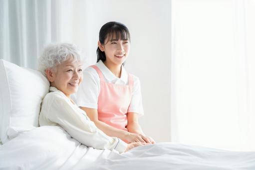 寝ているシニア女性を介護をする介護士 寝ているシニア女性を介護をする介護士の写真