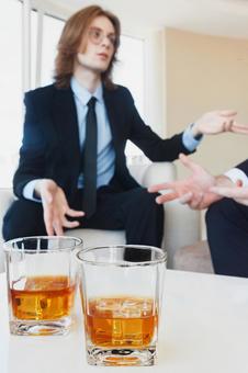 机に置かれた2個のグラスと長髪の男性 ウイスキーグラス,男性,座るの写真素材