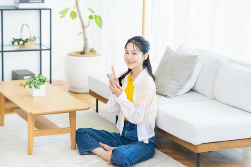 部屋でスマホを操作する女性 スマホ,笑顔,部屋の写真素材