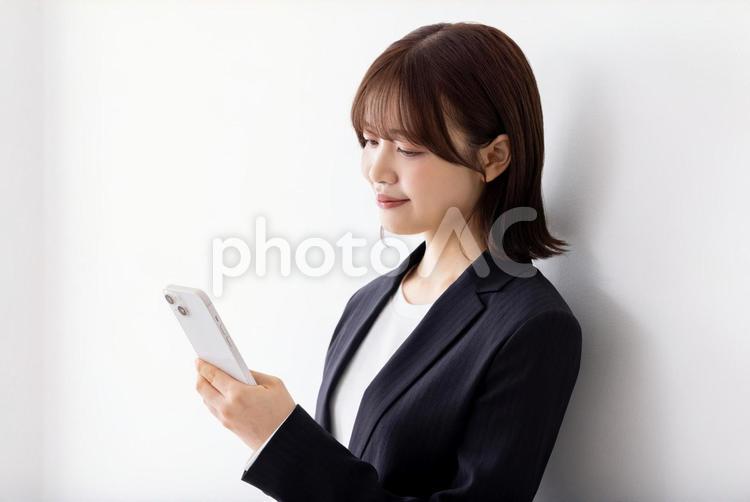 白壁に寄りかかりスマートフォンを使う女性 女性,ビジネスウーマン,スマートフォンの写真素材