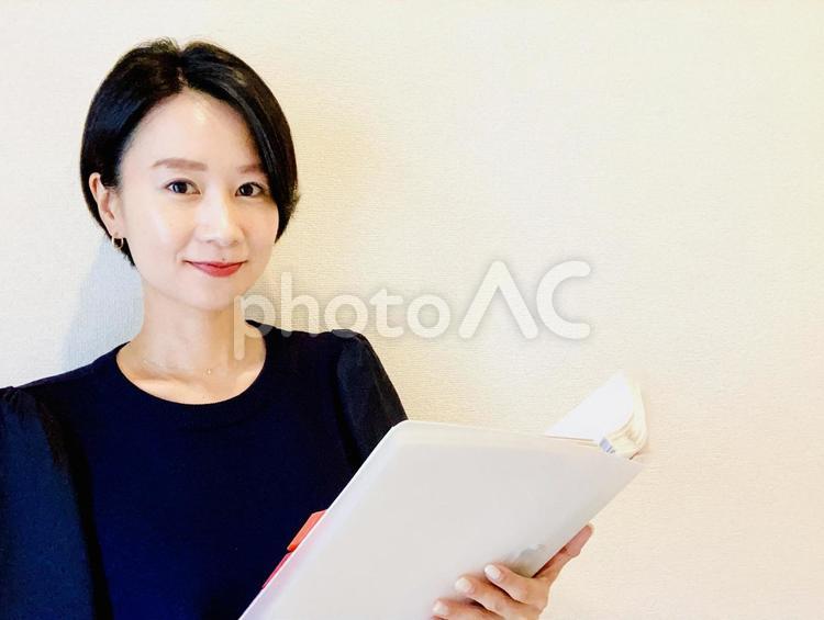 資料を見ながらカメラ目線で微笑む女性 女性,笑顔,微笑みの写真素材