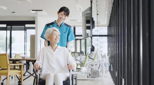 車椅子で散歩をする高齢者と介護士 車椅子で散歩をする高齢者と介護士の写真