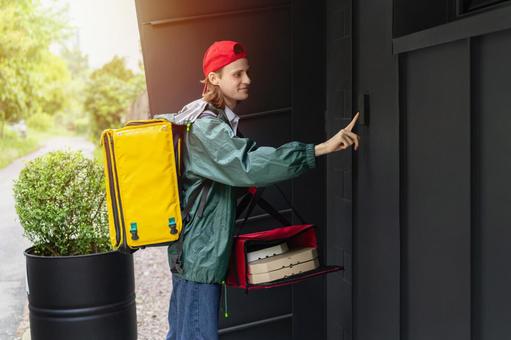 インターホンを押すピザデリバリーの男性の写真