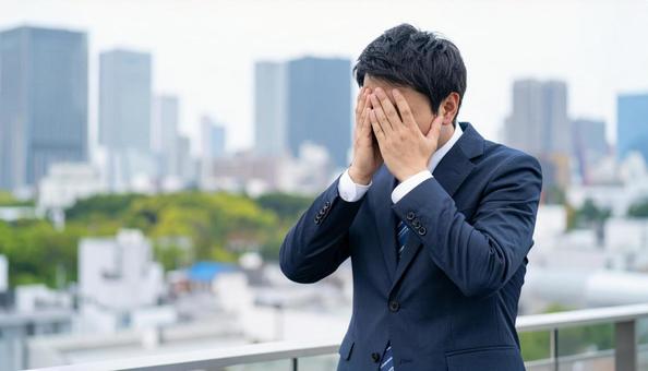 オフィスビルの屋上で苦悩するビジネスマンの写真