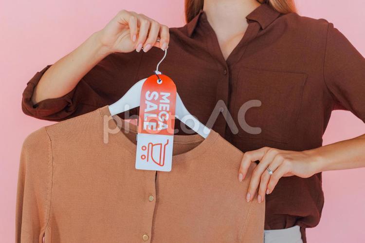 セールのタグの付いたハンガーに掛かった洋服を持っている女性 セール,ショップ,女性の写真素材