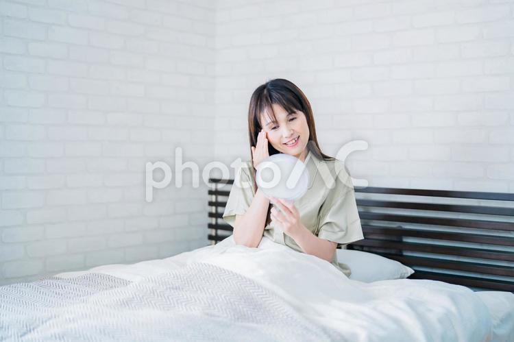 ベッドで鏡を見るミドル世代の女性（笑顔） アンチエイジング,睡眠,スキンケアの写真素材