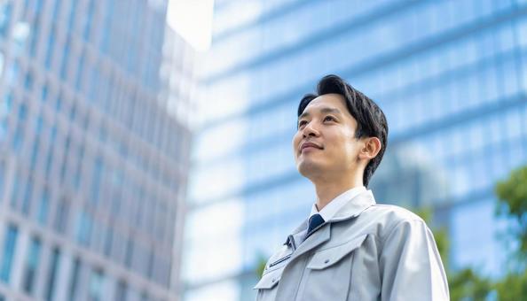 高層ビルの斜め上を見つめる若い作業服男性 高層ビルの斜め上を見つめる若い作業服男性の写真