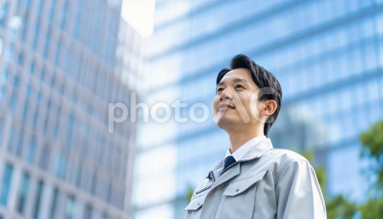 高層ビルの斜め上を見つめる若い作業服男性 男性,社会人,30代の写真素材